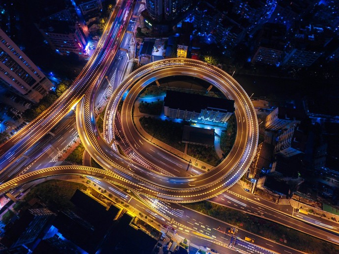 Aus der Luft heraus wird bei Nacht ein Straßennetz gezeigt, bei dem viele verschiedene Straßen kreuz und quer über-, unter- und nebeneinander laufen